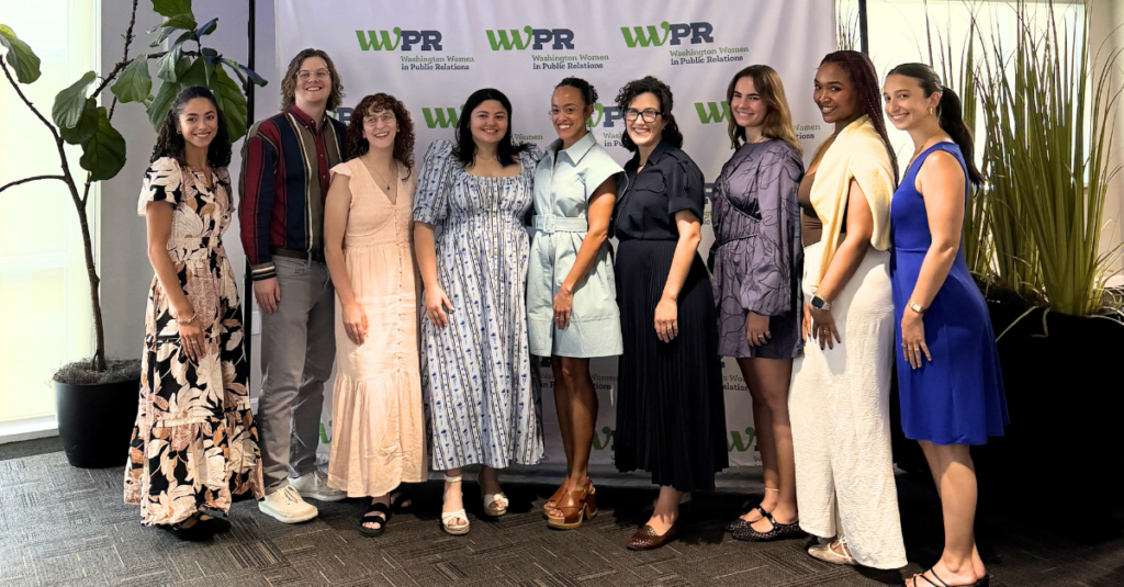 hive five graphics (10) Ten people stand smiling in front of a WNPR/WPR backdrop, dressed in business casual and semi-formal attire. Some wear dresses, others suits or coordinated outfits, perfectly embodying the energy of Summer 2026. Large plants decorate the left and right sides of the photo, capturing a moment featured in the Hive Five Newsletter.